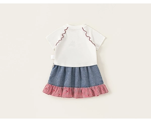 Detailed view of girls' white T-shirt with red stitching and denim patchwork skirt