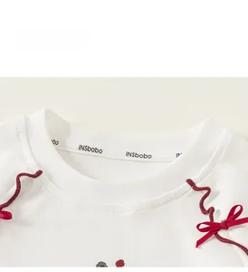 Detail of white cotton top neckline with red wavy ribbon accents and small decorative bows