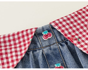 Macro shot of girl's denim dress featuring red gingham collar and cherry-shaped buttons