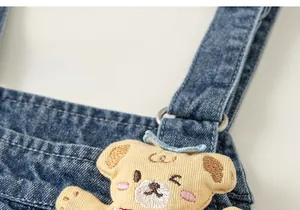 Detail of denim overalls with cute plush bear patch and metallic ring fasteners