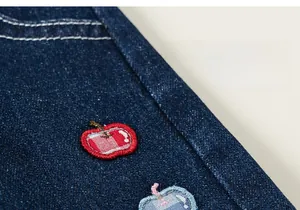 Détail du tissu denim délavé foncé avec broderie pomme et surpiqûres contrastées