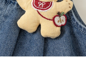 Detail of cute bear embroidery and small apple bag on blue denim overalls for girls