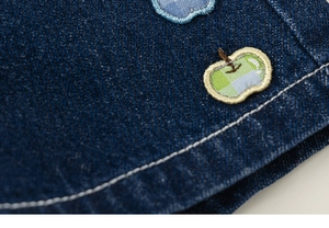 Détail macro du short en jean pour enfant avec broderie pomme et surpiqûres blanches