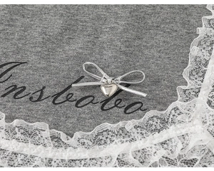 Detail of grey knitted T-shirt with heart pendant, silver bow and white lace trim