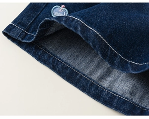 Détail du short en jean bleu foncé avec broderie pomme et surpiqûres blanches