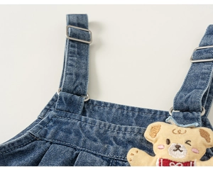 Detail of blue denim overalls showing metal buckles and cute cartoon bear embroidery
