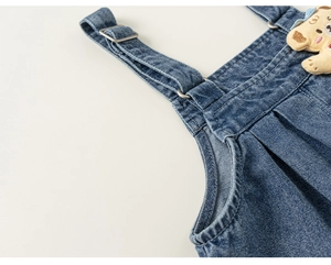 Detail shot of denim overalls with metal buckle and cute beige teddy bear ornament