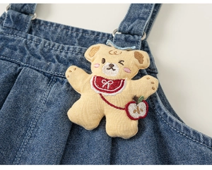Detail of blue denim overalls featuring a cute 3D knit bear patch with red apple embroidery