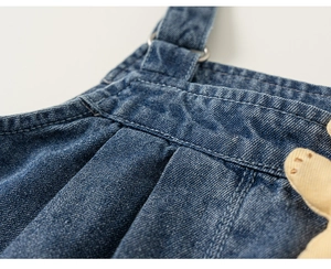 Detailed macro view of denim dungarees showing metal buckles and stitch texture
