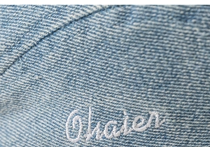 Macro detail of light blue washed denim beret featuring Chater letter embroidery