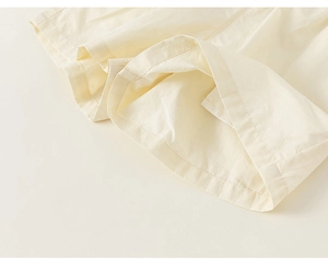 Detailed view of cream cotton fabric texture and precise hem stitching on kids' shorts