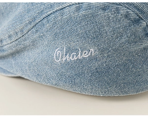 Detail shot of blue denim baby beret featuring white Ohaier embroidered lettering