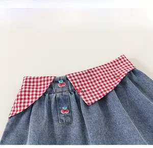 Détail de jupe en jean pour fille avec carreaux rouges et bouton cerise mignon