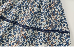 Dettaglio del tessuto floreale blu con bordo in pizzo traforato su un vestito estivo da bimba