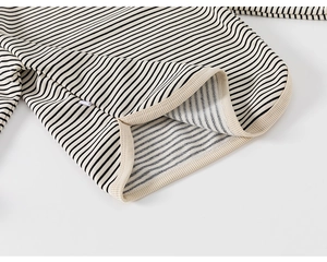 Detailed close-up of ribbed cuffs and hem on a black and white striped cotton knit sweater