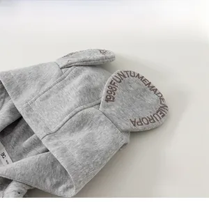 Detail of grey infant hoodie featuring 3D cartoon ears with brown letter embroidery