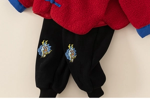 Détail du haut en polaire rouge à boutons bleus et broderie de dragon sur le pantalon noir