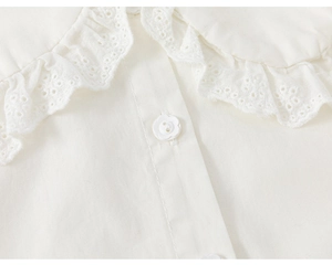 Close-up of white girls shirt showing ruffled eyelet lace collar and flower-shaped buttons