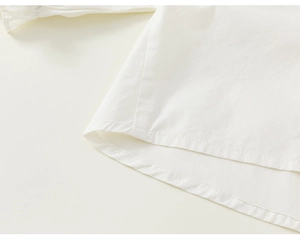 Detailed close-up of the clean hem stitching on a white cotton girl's ruffle blouse