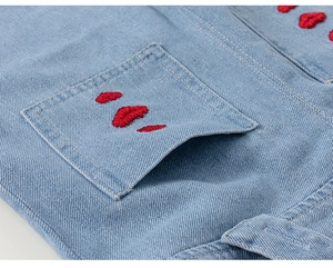 Nahaufnahme von hellblauem Denimstoff mit roter Lippenbestickung und feiner Twill-Textur