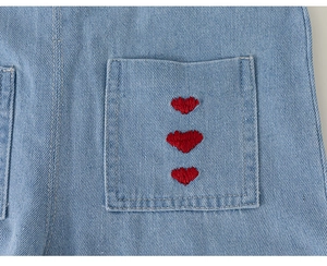 Detailaufnahme von blauem Denim-Stoff mit drei roten Herzstickereien auf der Tasche