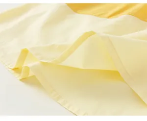 Detailed close-up of the fine double-stitch sewing and hem finish on the yellow cotton dress