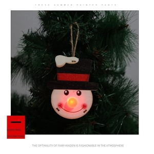 Close-up of a wooden snowman Christmas ornament with a glowing LED nose on a tree branch