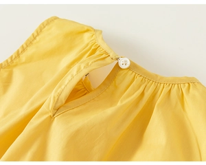 Macro detail of yellow cotton girl's dress with back button closure and pleated neckline