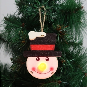 Detail of wooden snowman Christmas ornament with LED nose on a tree branch