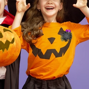 Detail of Halloween ID badge reel with black spider web and purple bat on pumpkin shirt