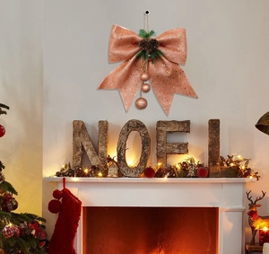 Rose gold glitter Christmas bow with pine cones hanging on a warm cozy fireplace