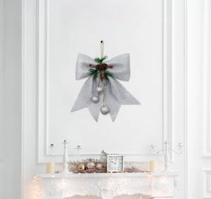Silver glitter Christmas bow with pine cones and red berries on a white fireplace wall