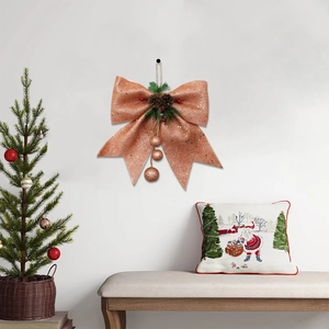 Rose gold Christmas bow ornament with pine cones, needles and glitter balls on white wall