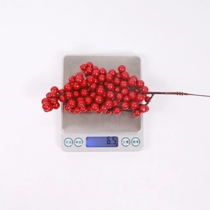 Detail showing artificial red berries on a digital scale weighing exactly 6.5 grams