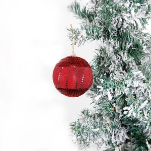 Festive red Christmas ball with silver sequins hanging on a snowy pine tree branch