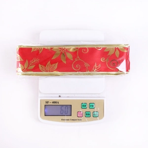 Detail of red Christmas ribbon with golden floral print and wired edges on a scale