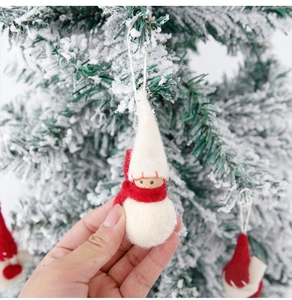 Handmade white wool felt Christmas gnome ornament with red scarf hanging on a snowy tree