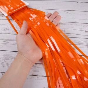 Detail of glossy orange fringe curtain showing metallic reflection and high density material