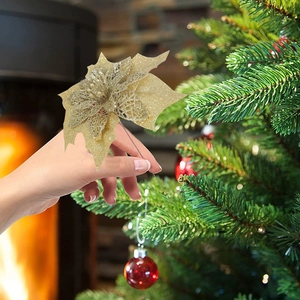Détail d'une main plaçant un poinsettia doré pailleté sur un sapin de Noël décoré
