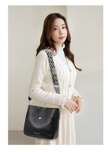 Detail of black pebbled leather crossbody bag with striped wide fabric strap and metal clasp