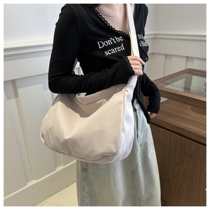 Detail of a beige crescent canvas crossbody bag worn by a model in a minimalist setting