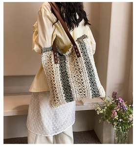 Detail of hand-woven straw tote bag with brown leather straps and white stitching
