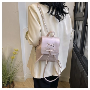 Detail of light pink mini backpack featuring decorative bow and chain straps on model