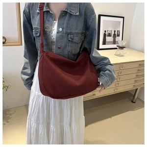 Close-up of a burgundy canvas crossbody bag worn with a casual denim outfit and white skirt
