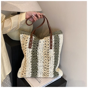 Detail of green and white woven straw tote with brown faux leather handles and stitching