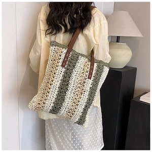 Close-up of green and beige woven straw tote bag with brown leather shoulder straps