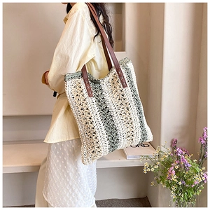 Detail view of woven straw shoulder bag with green stripes and brown leather strap