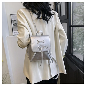 Rear view of model wearing a mini silver metallic backpack with bow and chain detail