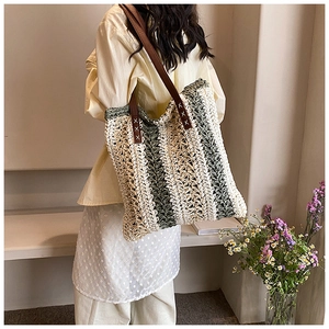 Close-up of woven straw tote bag with green stripes and brown leather shoulder strap