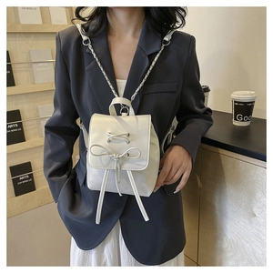 Detailed view of white mini PU leather backpack with bow drawstring and chain strap on model